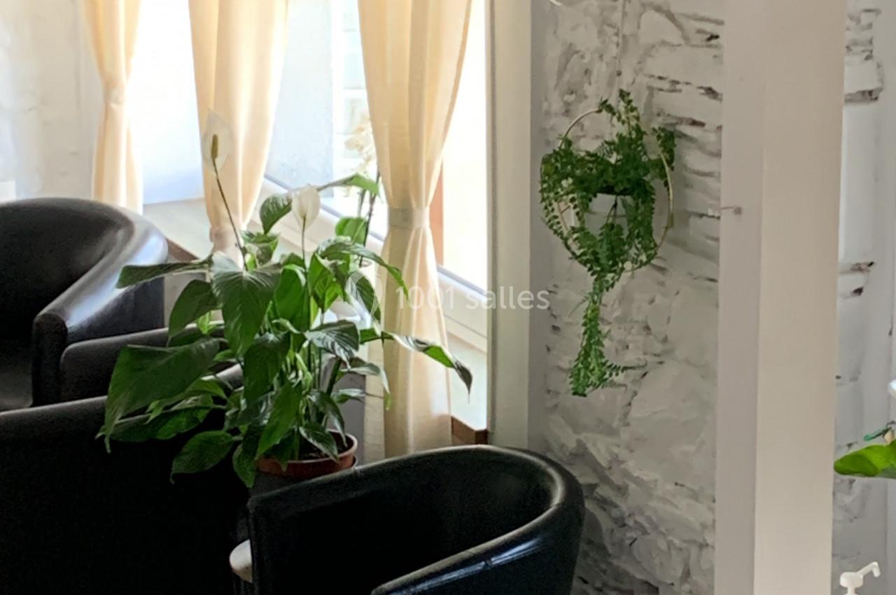 Deux fauteuils noirs près d'une table basse, entourés de plantes et éclairés par une lumière naturelle.