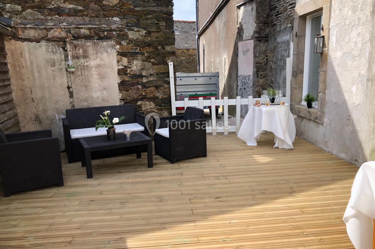 Terrasse en bois avec mobilier de jardin, table dressée et murs en pierre dans une cour extérieure.