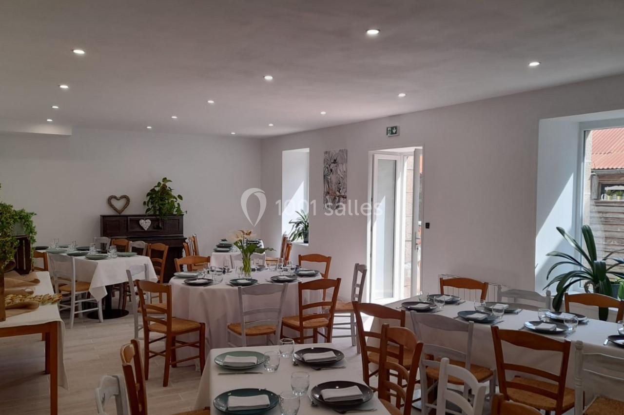 Salle lumineuse aménagée pour un repas, avec tables dressées, chaises en bois et décoration végétale.