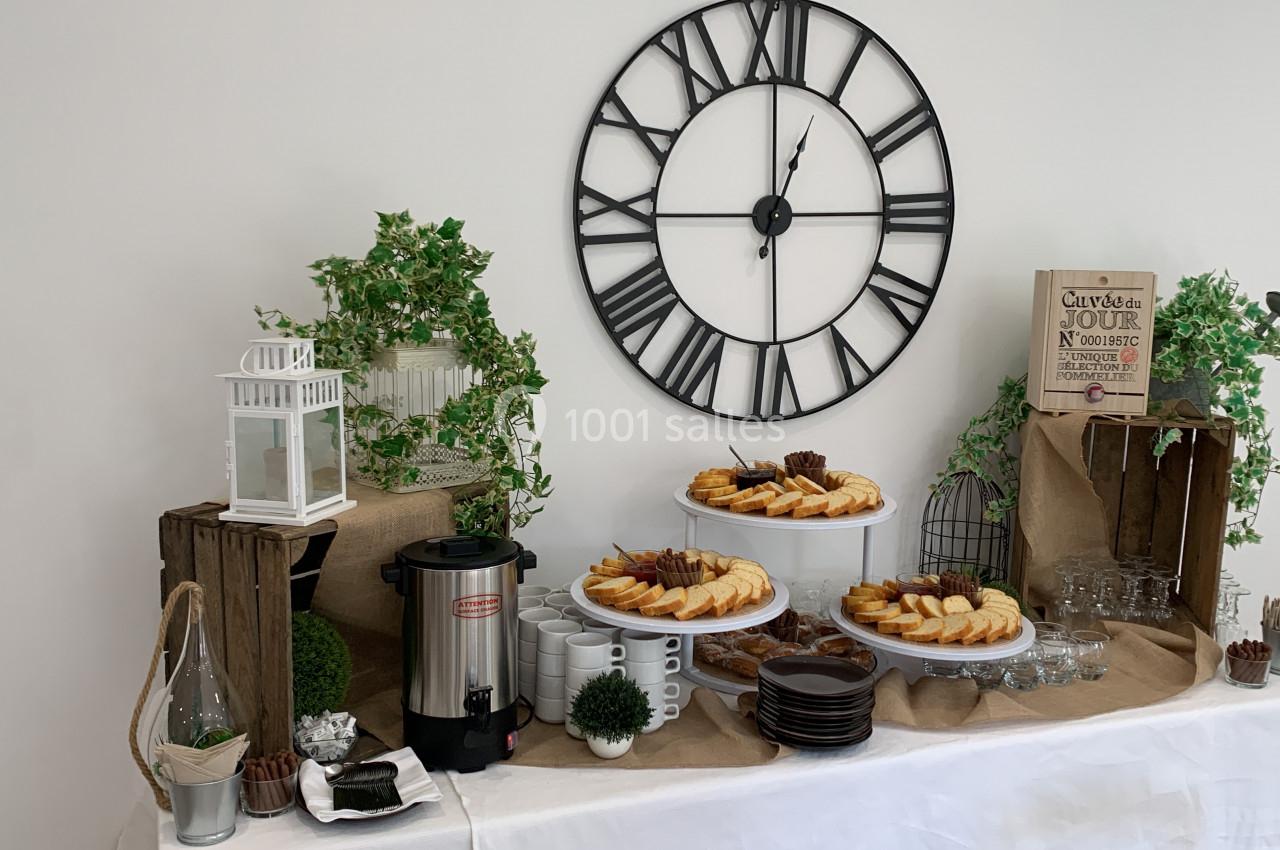 Buffet décoratif avec gâteaux, cafetière, vaisselle et éléments végétaux sous une grande horloge murale.