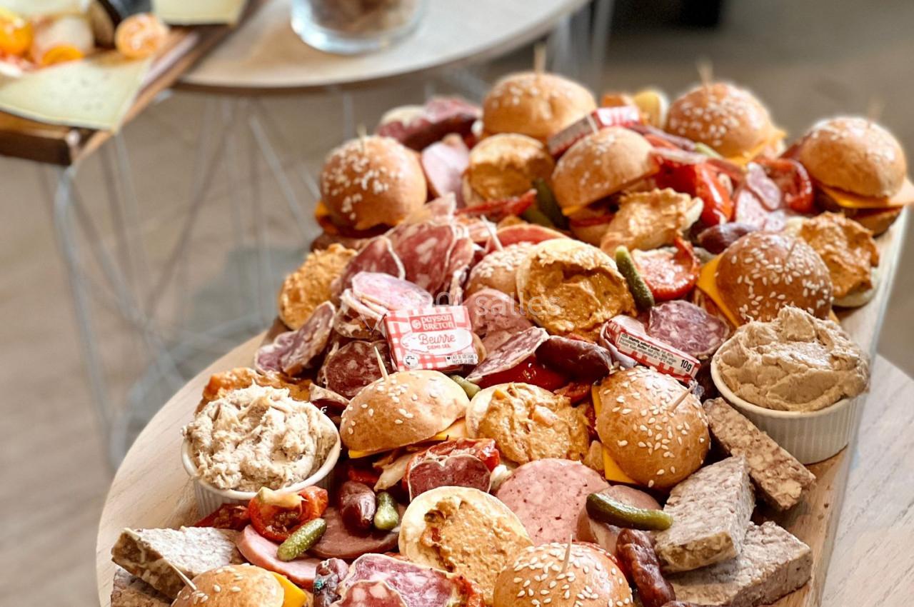 Plateau garni de mini-sandwichs, charcuteries, fromages et accompagnements sur une table en bois.