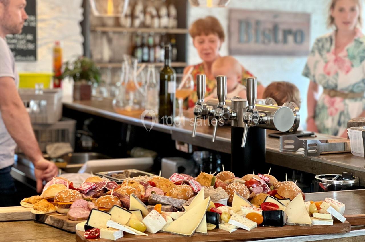 Plateau de fromages et charcuteries variés sur un comptoir de bistrot, avec des personnes en arrière-plan.