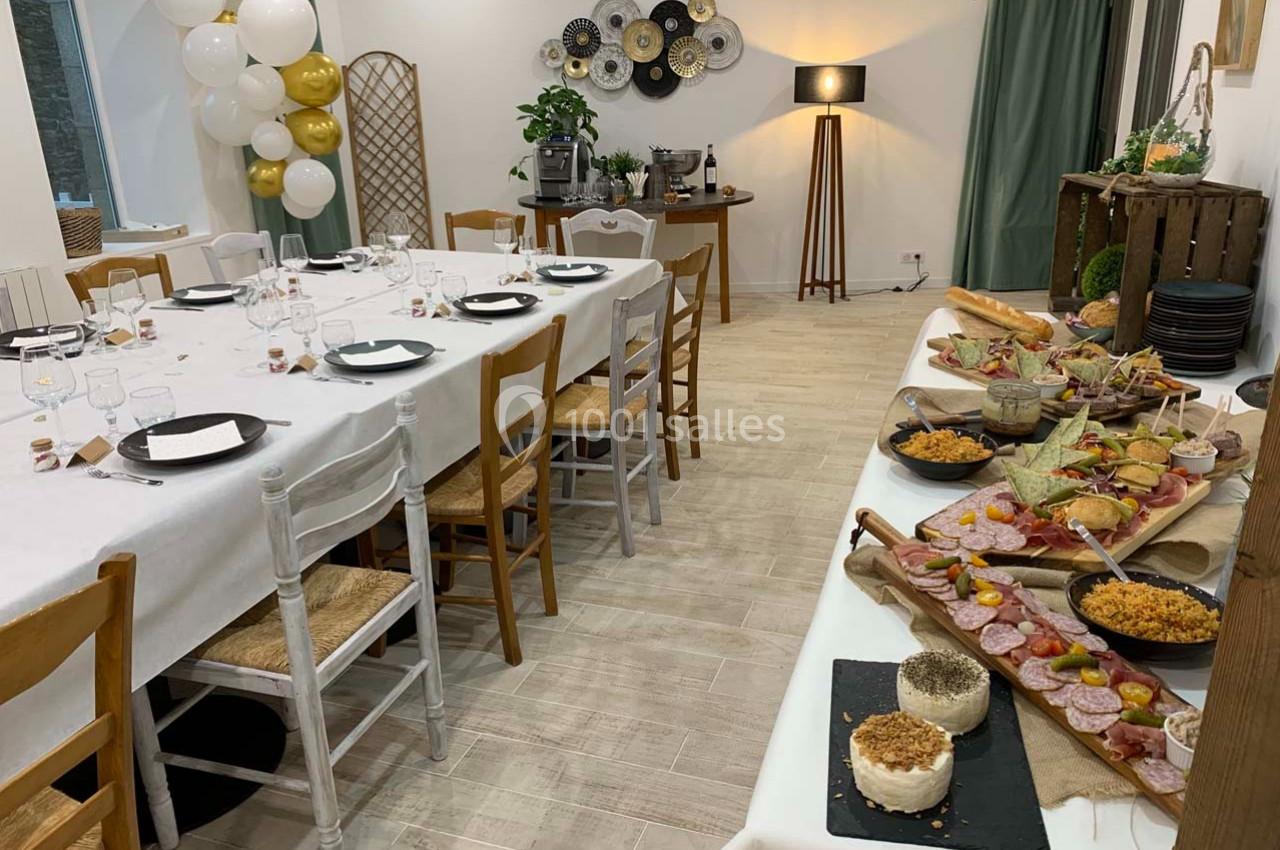 Salle décorée pour un événement avec tables dressées, buffet de charcuterie et fromages, et ballons en arrière-plan.