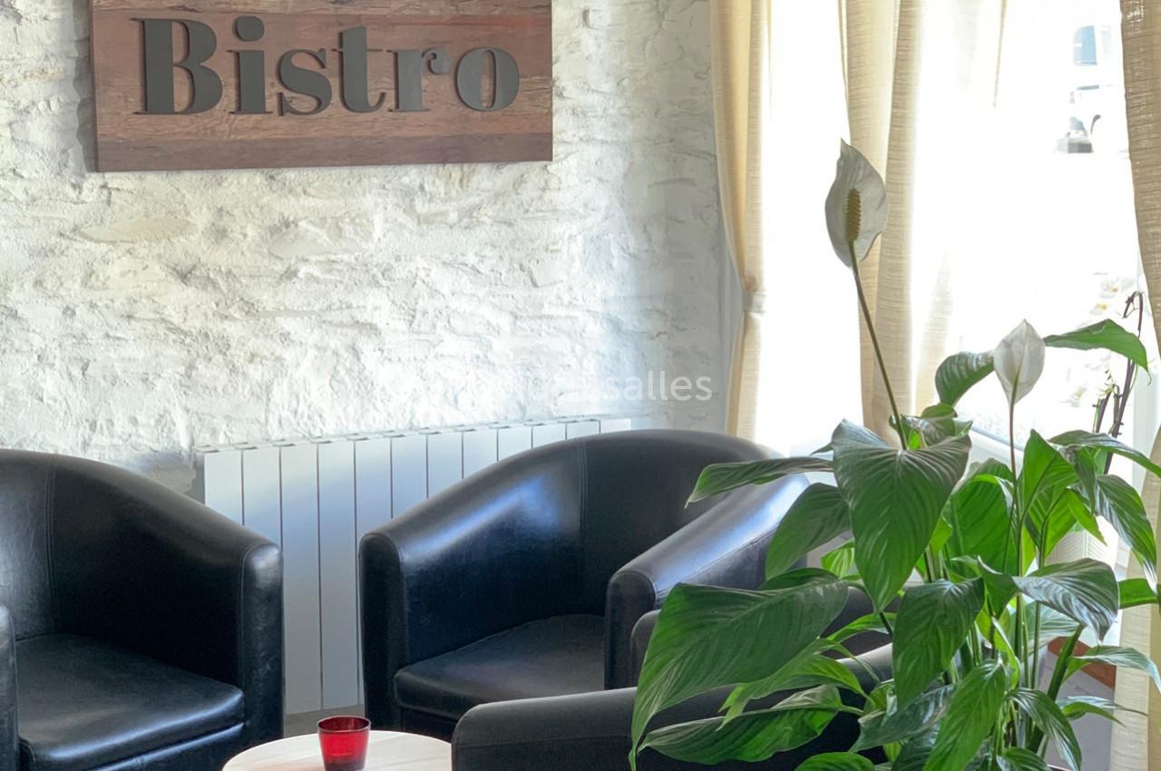 Coin salon avec deux fauteuils noirs, une petite table ronde, une plante verte et un panneau ’Bistro’ sur un mur blanc.