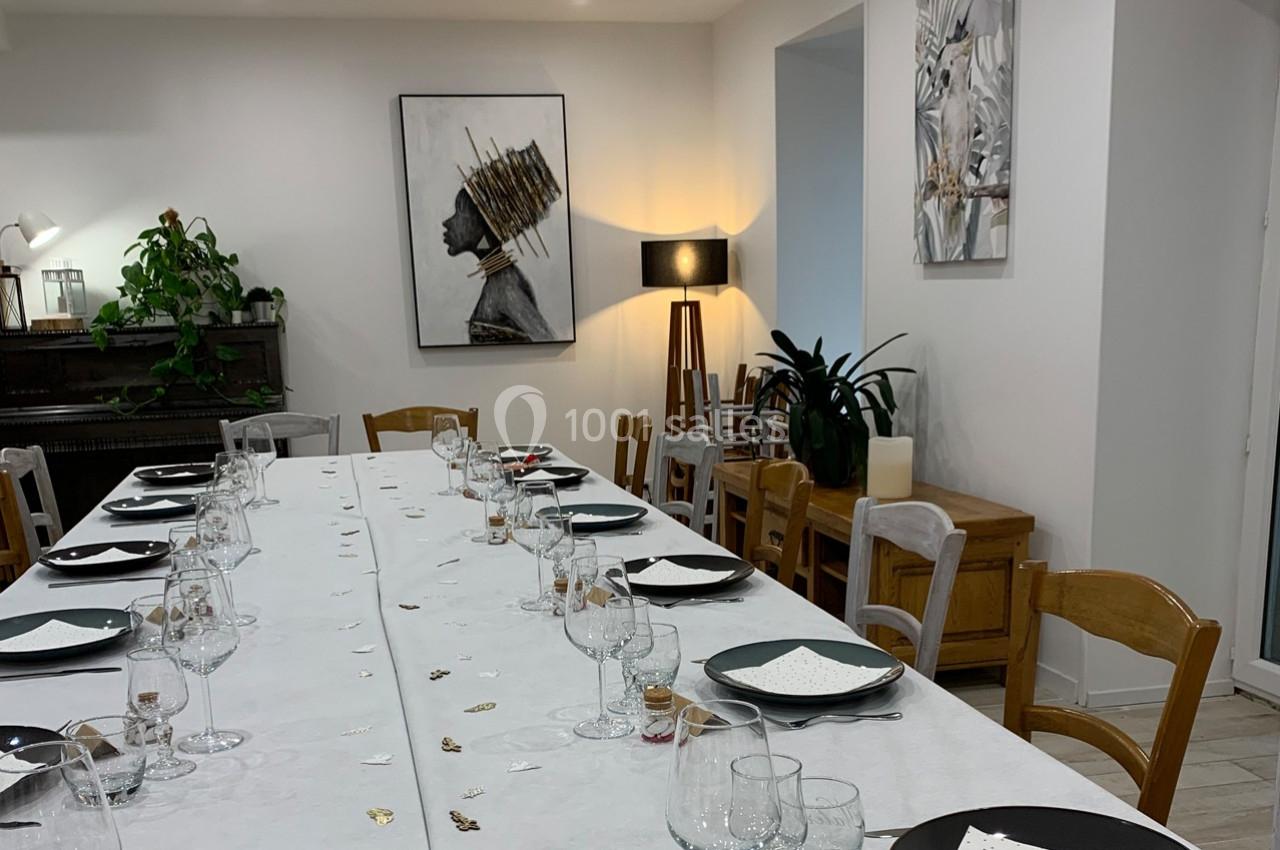 Table dressée avec vaisselle et décorations dans une salle lumineuse, ornée de plantes et de tableaux modernes.