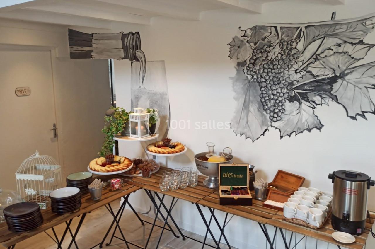 Table de buffet avec viennoiseries, boissons chaudes, verres et décoration murale représentant des grappes de raisin.