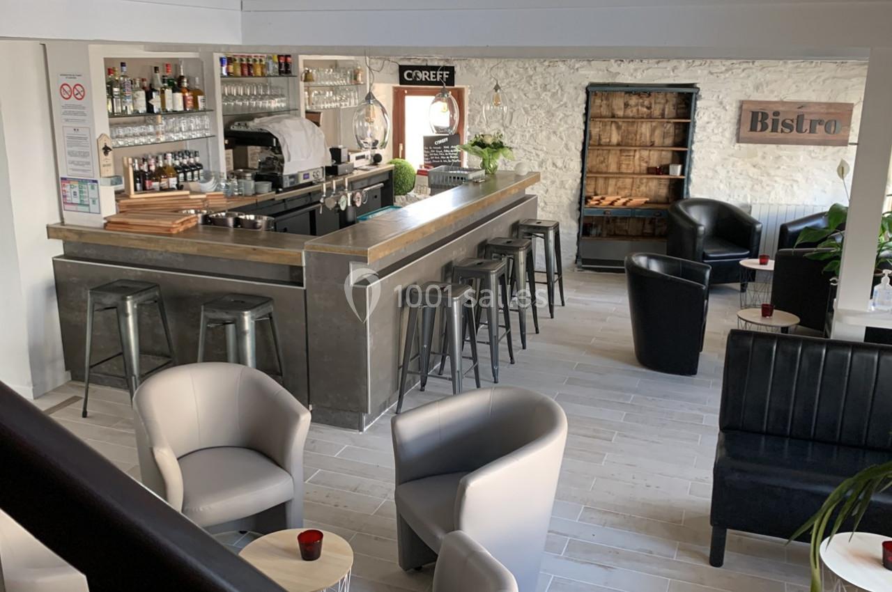 Intérieur d'un bar moderne avec comptoir, tabourets hauts, fauteuils, et décoration murale en pierre apparente.