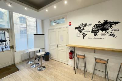 Salle de classe lumineuse avec des tables et chaises noires alignées, un projecteur suspendu et une grande fenêtre.