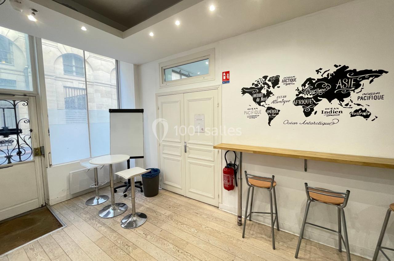 Salle lumineuse avec tables hautes, chaises, tableau blanc et décoration murale représentant une carte du monde.