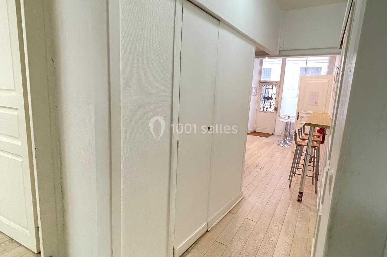 Couloir lumineux avec parquet clair, placards intégrés et vue sur une pièce avec table et chaises près d'une fenêtre.