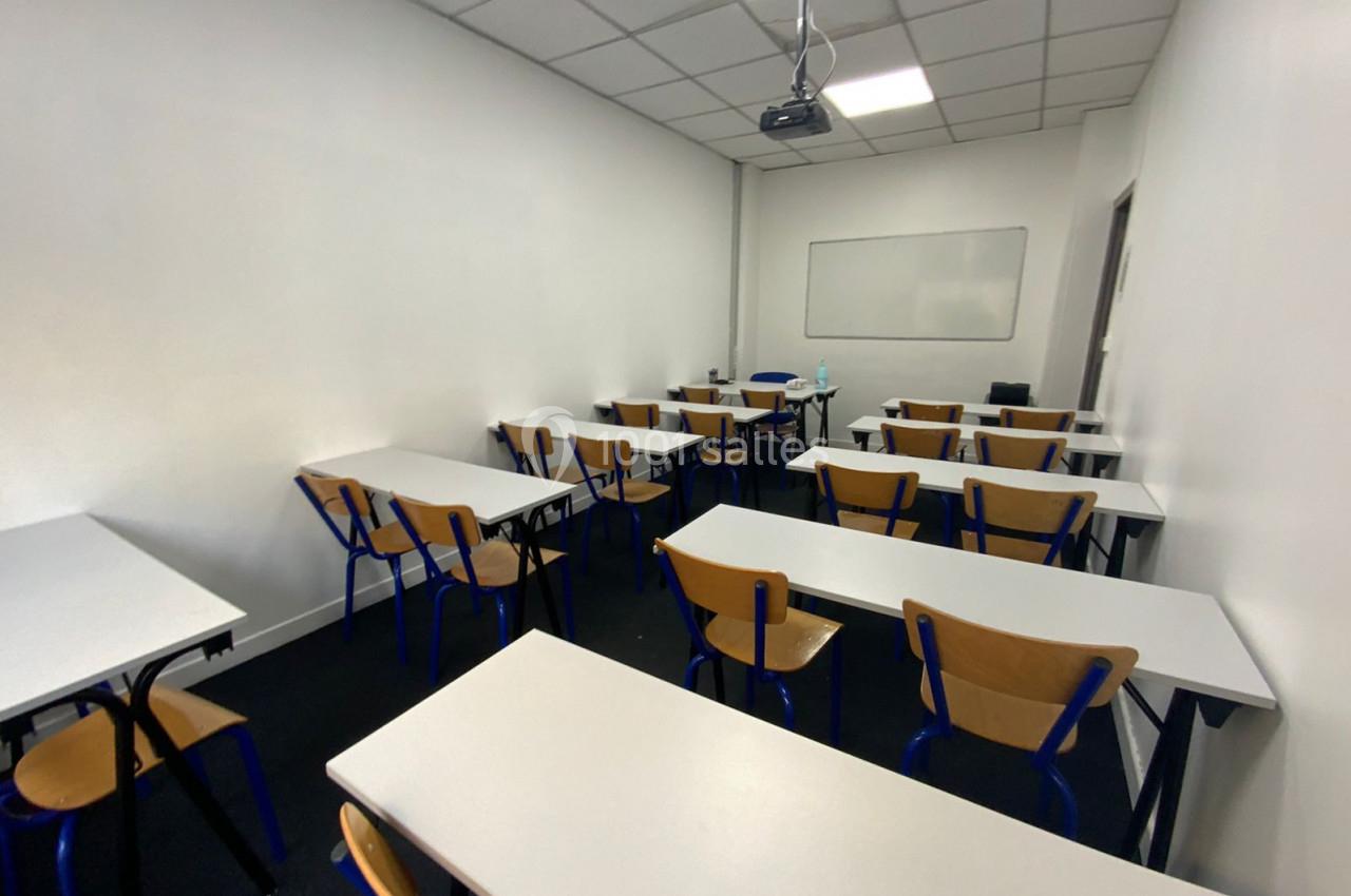 Salle de classe vide avec des tables, des chaises en bois et un tableau blanc au mur.