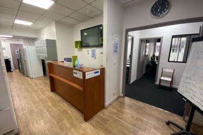 Salle de classe lumineuse avec des tables et chaises noires alignées, un projecteur suspendu et une grande fenêtre.
