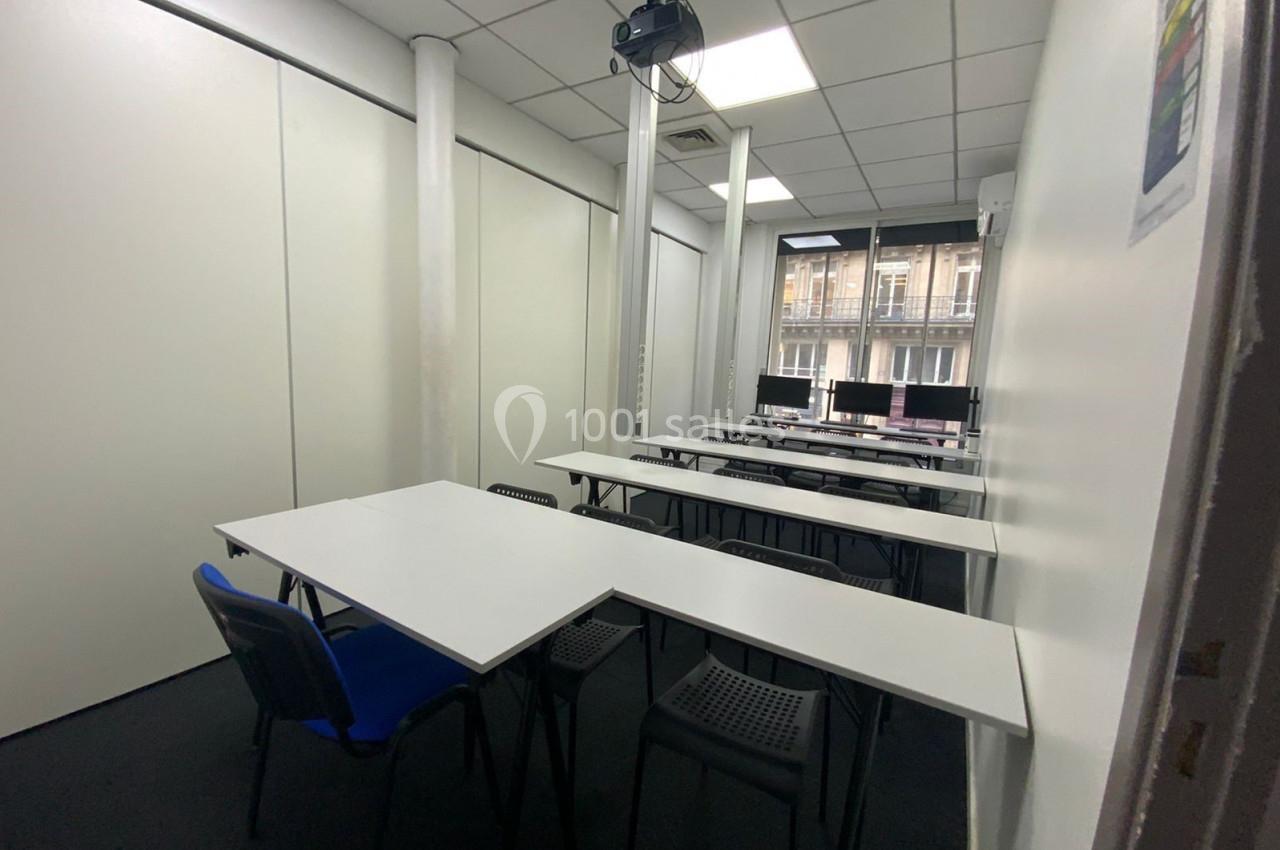 Salle de formation équipée de tables, chaises, projecteur au plafond et ordinateurs près d'une fenêtre.