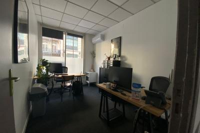 Salle de classe lumineuse avec des tables et chaises noires alignées, un projecteur suspendu et une grande fenêtre.