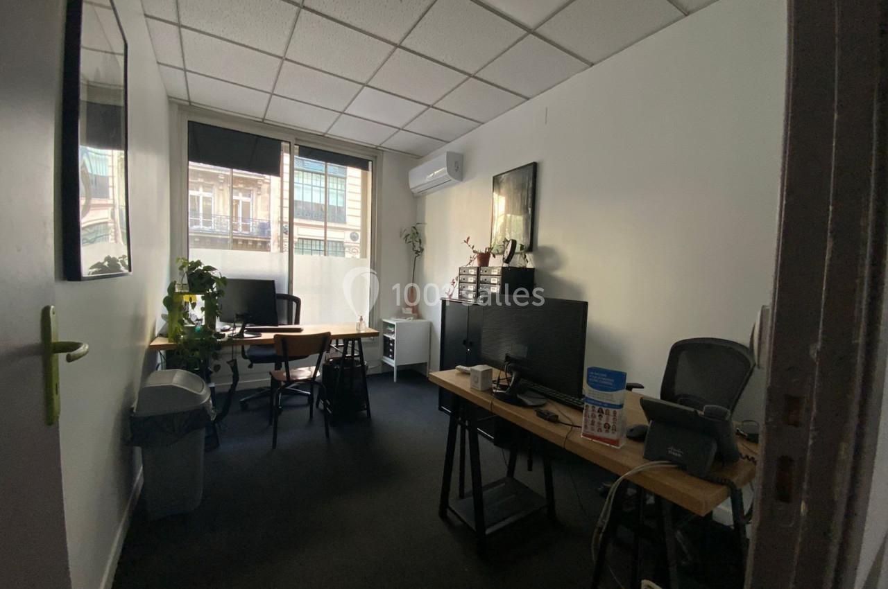 Bureau lumineux avec deux postes de travail, des plantes, des étagères et une fenêtre donnant sur des immeubles.