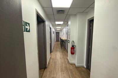 Salle de classe lumineuse avec des tables et chaises noires alignées, un projecteur suspendu et une grande fenêtre.