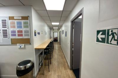Salle de classe lumineuse avec des tables et chaises noires alignées, un projecteur suspendu et une grande fenêtre.
