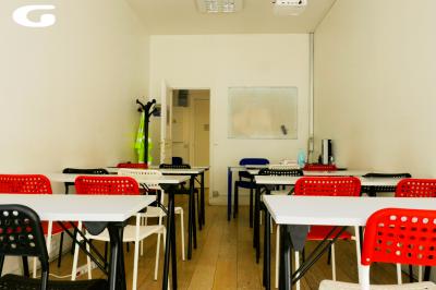 Salle de classe lumineuse avec des tables et chaises noires alignées, un projecteur suspendu et une grande fenêtre.