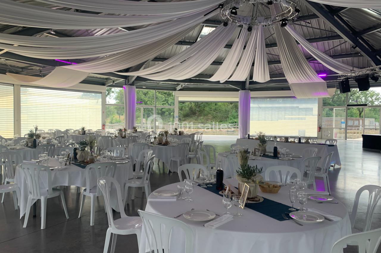Salle de réception lumineuse avec des tables rondes dressées, des nappes blanches et des drapés suspendus au plafond.