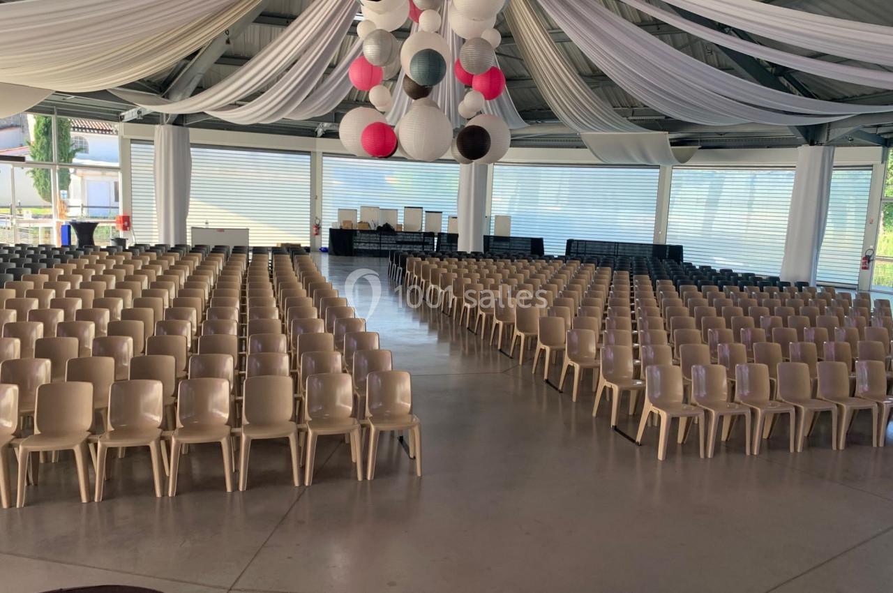Salle lumineuse aménagée avec des rangées de chaises beiges, décorée de guirlandes et de lanternes suspendues.