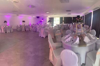 Allée centrale bordée de chaises blanches menant à une arche décorée de fleurs, dans un cadre extérieur arboré.