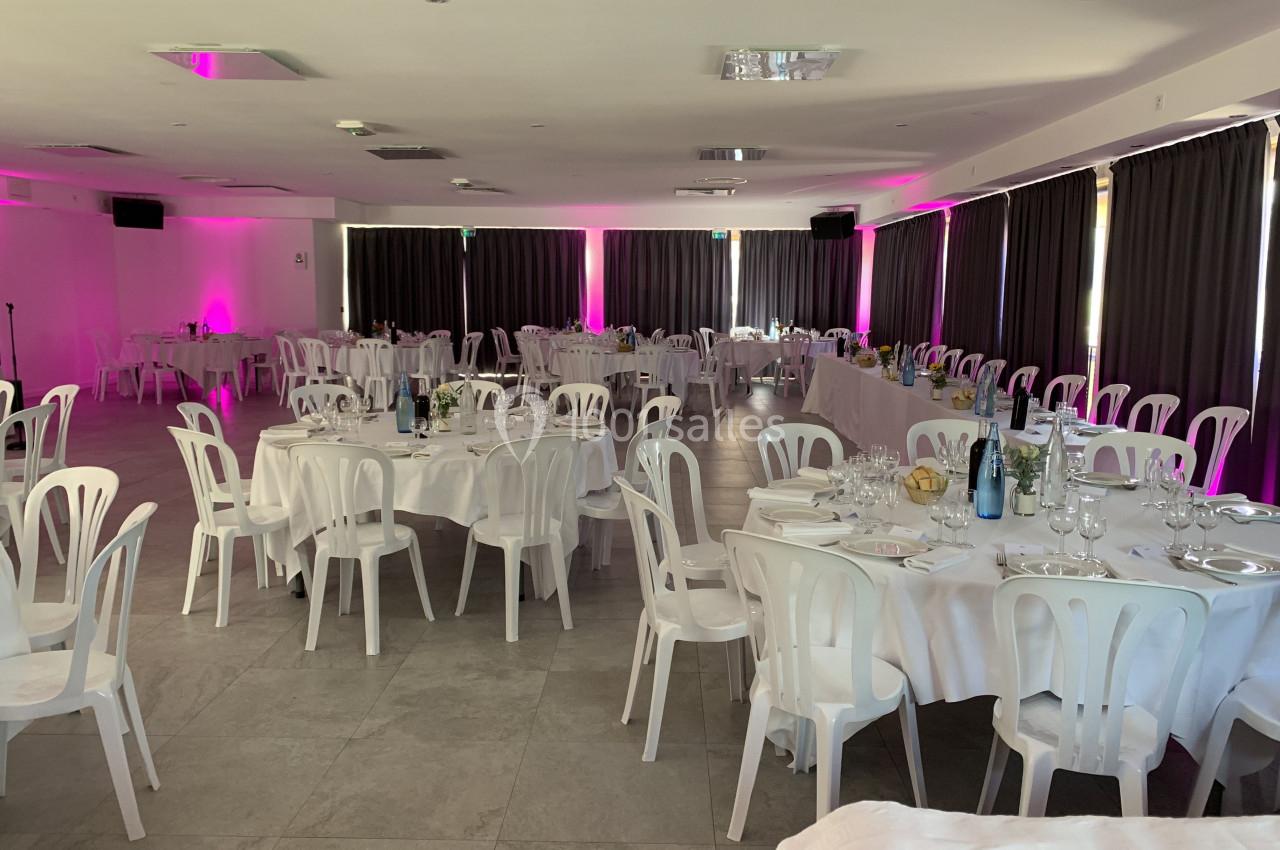 Salle de réception avec tables rondes et rectangulaires dressées, éclairage tamisé et rideaux sombres.