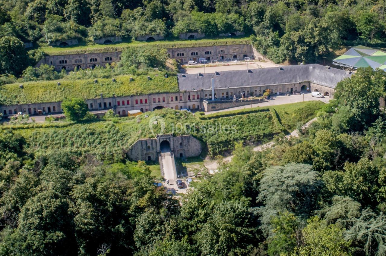 Vue aérienne d'un fort entouré de végétation dense, avec bâtiments en pierre et structures couvertes visibles.
