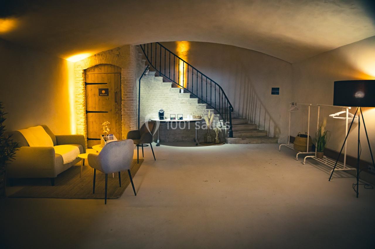 Espace intérieur avec canapé, chaises, escalier en pierre, éclairage chaleureux et éléments décoratifs.