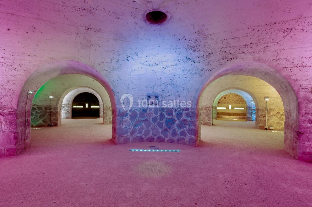 Intérieur d'une structure voûtée en pierre, éclairée par des lumières colorées roses, bleues et vertes.