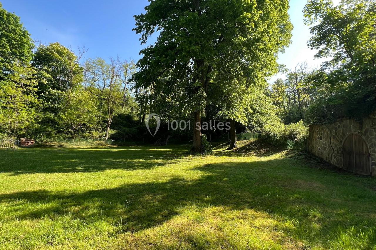 Pelouse ensoleillée entourée d'arbres et d'un mur en pierre avec une porte en bois, par une journée claire.