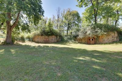Deux structures en pierre recouvertes de végétation dans un espace herbeux entouré d'arbres.