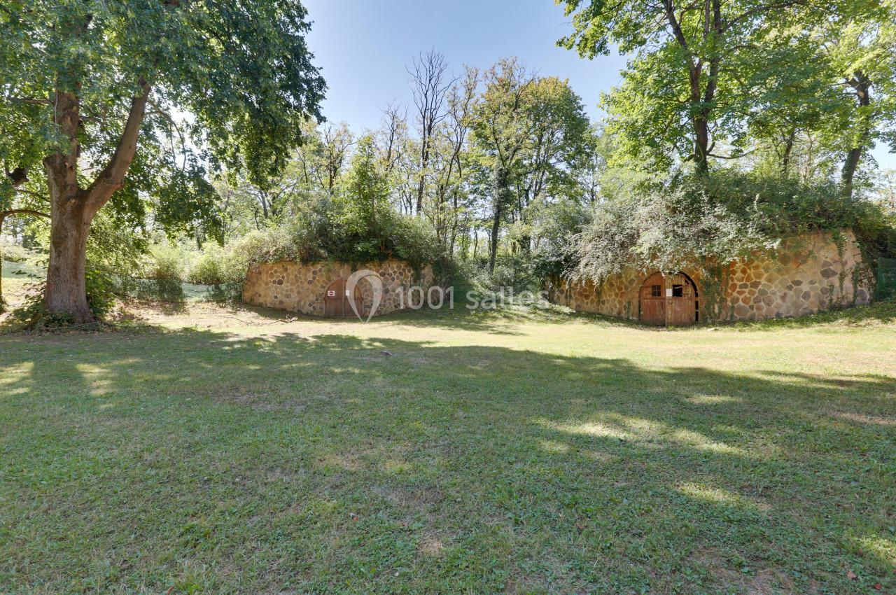 Deux structures en pierre recouvertes de végétation dans un espace herbeux entouré d'arbres.