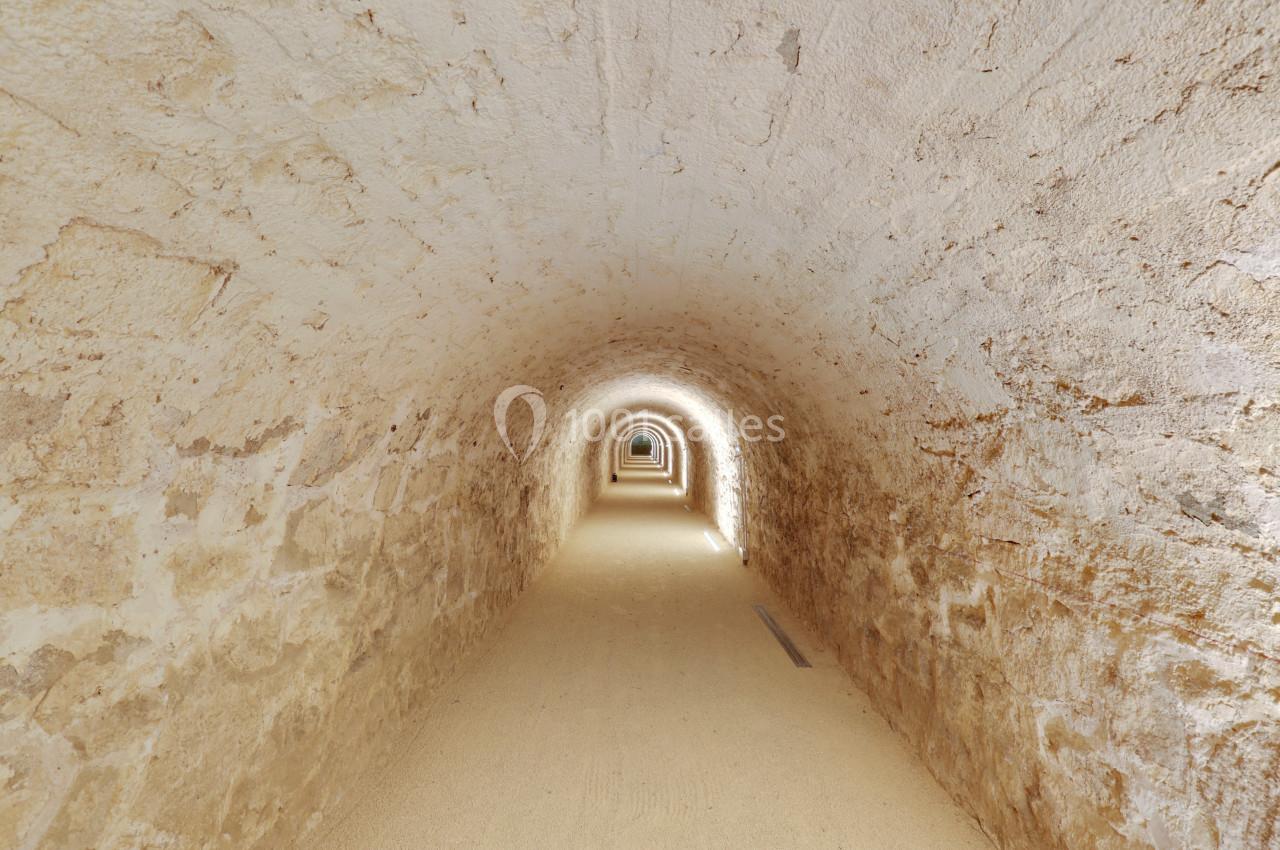 Vue d'un long tunnel en pierre aux parois claires, éclairé par des lumières discrètes au sol.