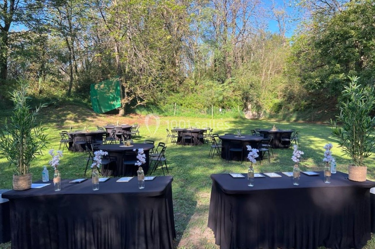 Tables noires décorées de vases fleuris disposées en extérieur sur une pelouse entourée d'arbres.