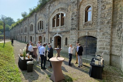 Serveur portant un plateau dans un événement en plein air sous des tentes, avec des invités assis et debout.