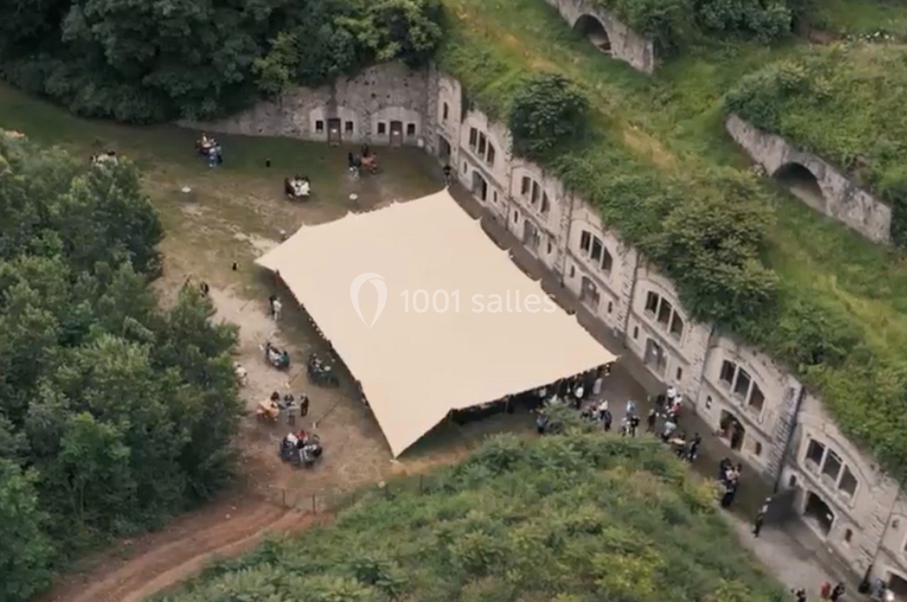 Vue aérienne d'une structure en toile beige installée dans une cour entourée de murs en pierre et de végétation.