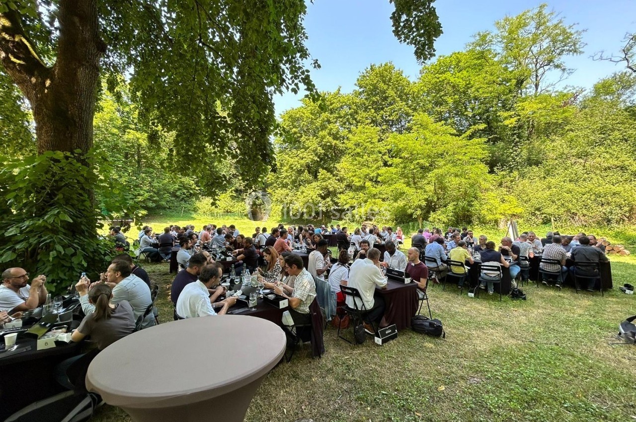Groupe de personnes assises à des tables en plein air dans un cadre verdoyant, lors d'un événement convivial.