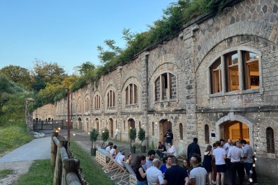Serveur portant un plateau dans un événement en plein air sous des tentes, avec des invités assis et debout.