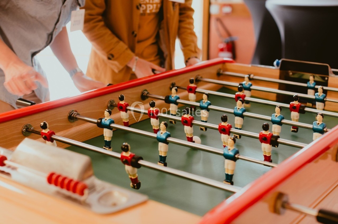Personnes jouant à un baby-foot avec des figurines rouges et bleues dans un cadre intérieur.