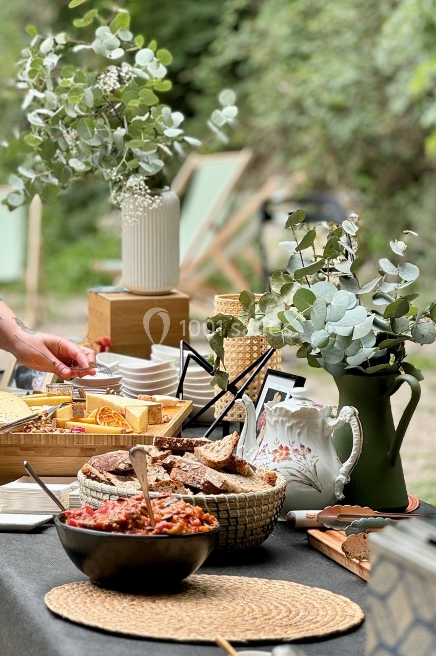 Buffet en plein air avec des plats variés, des fleurs en vase et une ambiance naturelle entourée de verdure.