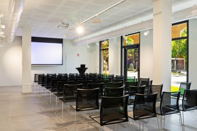 Salle de réunion en pierre avec table rectangulaire, chaises noires, rétroprojecteur, écran blanc et tableau de conférence.