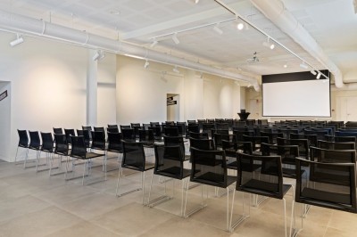 Salle de réunion en pierre avec table rectangulaire, chaises noires, rétroprojecteur, écran blanc et tableau de conférence.