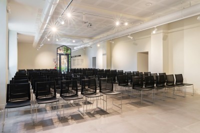 Salle de réunion en pierre avec table rectangulaire, chaises noires, rétroprojecteur, écran blanc et tableau de conférence.