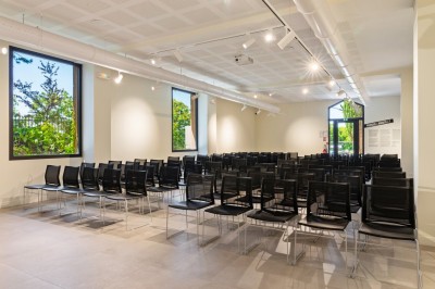 Salle de réunion en pierre avec table rectangulaire, chaises noires, rétroprojecteur, écran blanc et tableau de conférence.