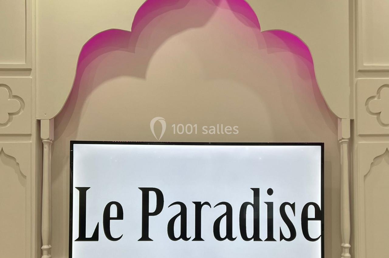 Panneau lumineux avec l'inscription ’Le Paradise’ sur un mur décoré d'une arche rose et blanche.