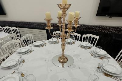 Salle lumineuse avec miroir doré, tabouret, banc noir, portant à vêtements et tableau décoratif sur un mur blanc.