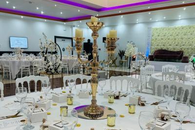 Salle lumineuse avec miroir doré, tabouret, banc noir, portant à vêtements et tableau décoratif sur un mur blanc.