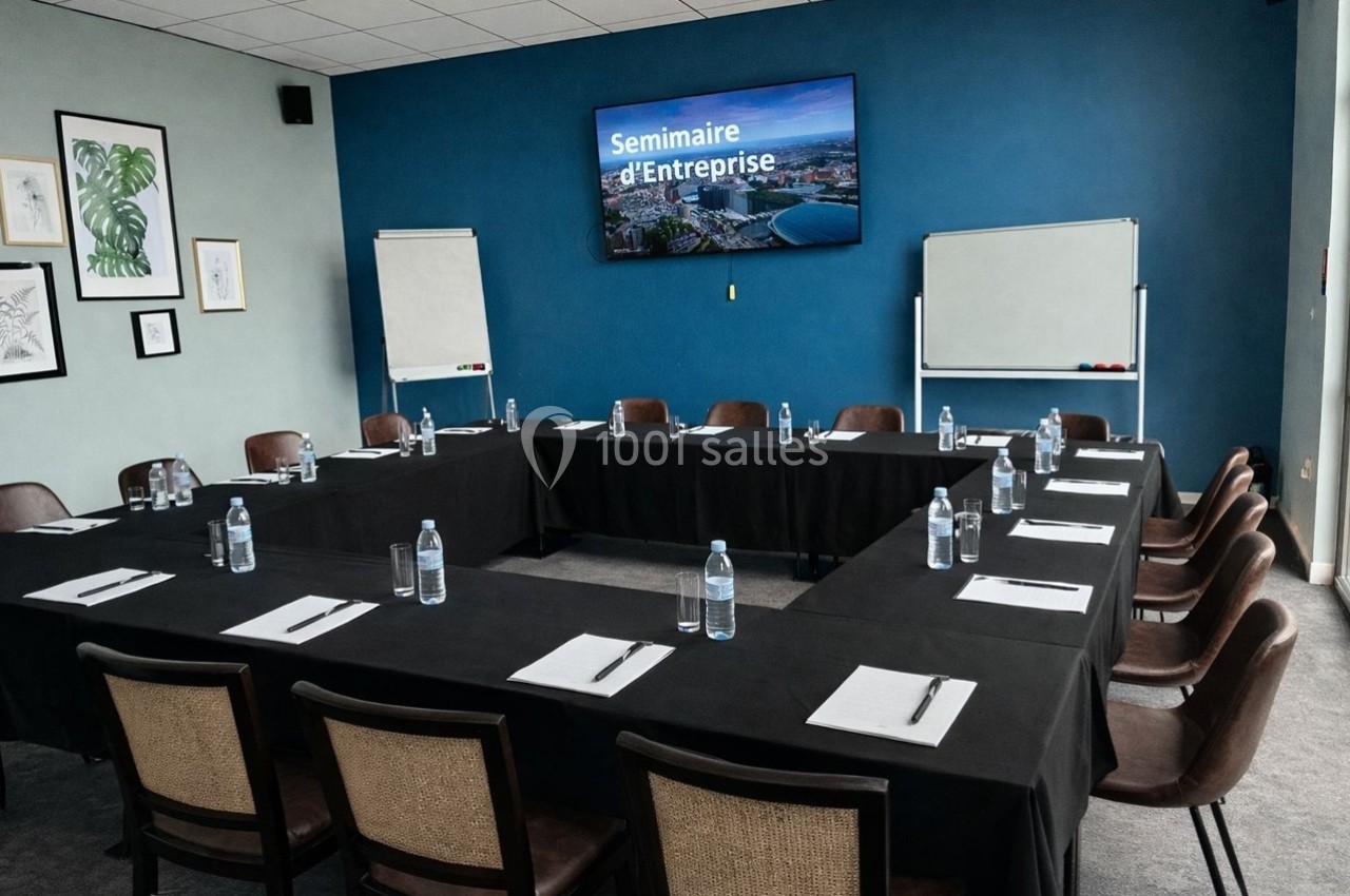 Salle de réunion avec tables en U, chaises, blocs-notes, bouteilles d'eau et écran affichant ’Séminaire d'Entreprise’.
