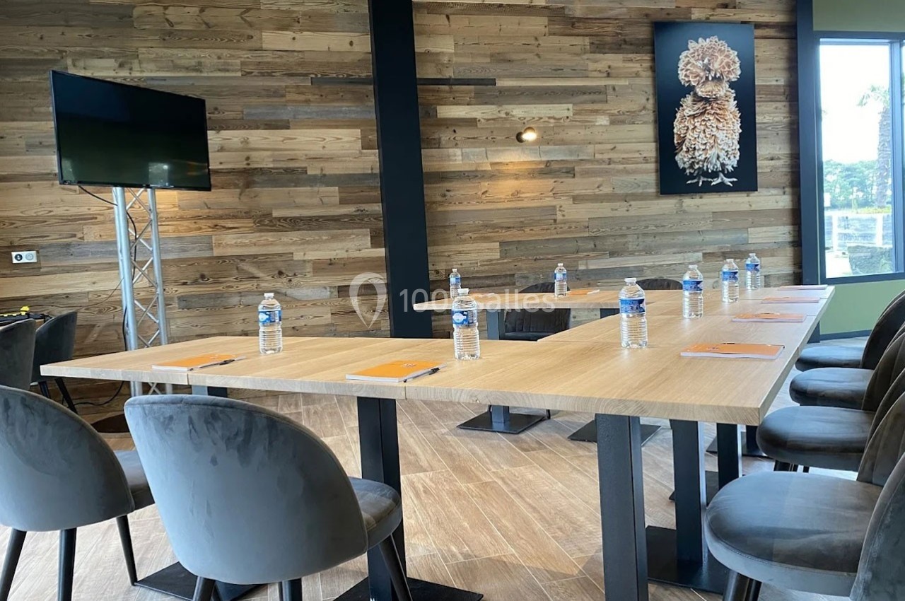 Salle de réunion moderne avec tables en bois, chaises grises, bouteilles d'eau et carnets disposés pour les participants.