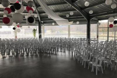 Kiosque en toit de chaume entouré d'arbres, situé dans une cour pavée avec des voiles d'ombrage.
